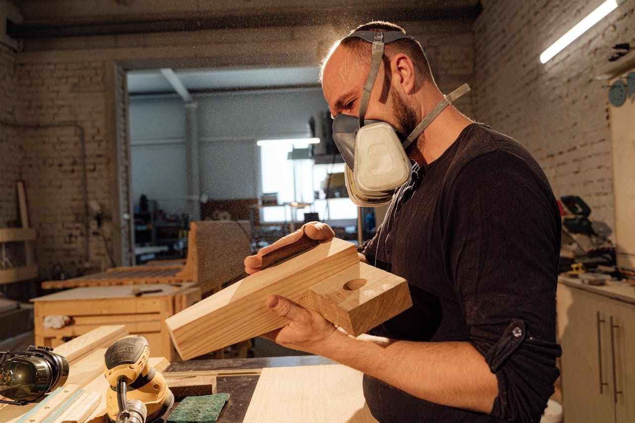 Skilled carpenter wearing mask, shaping wood with tools in a workshop environment.